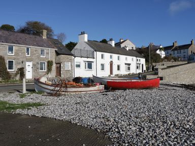Boats on a pebble shore in front of stone and white houses at Bwthyn in Moelfre
