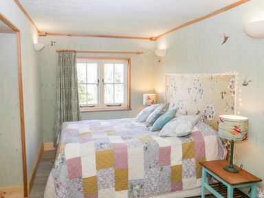A bedroom with a bed covered with a patchwork quilt and pillows next to a small wooden side table with a lamp at Little Willow in Farrington near Child Okeford