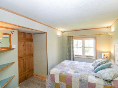 A bedroom with a wooden door a bed with a patchwork quilt and pillows and a window with curtains at Little Willow in Farrington near Child Okeford