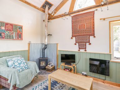 A living room with a wood stove a plaid armchair a coffee table a small tv and decorative wall hangings at Little Willow in Farrington near Child Okeford