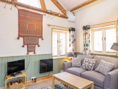 A living room with a sofa a coffee table a small television on a wooden stand and patterned curtains at Little Willow in Farrington near Child Okeford