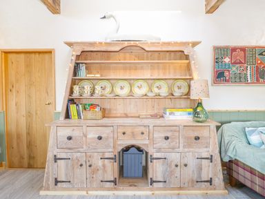 A wooden cabinet with dishes books a lamp and a swan decoration in a room at Little Willow in Farrington near Child Okeford
