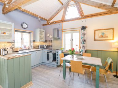 A kitchen with a dining table chairs flowers on the table and wooden beams at Little Willow in Farrington near Child Okeford