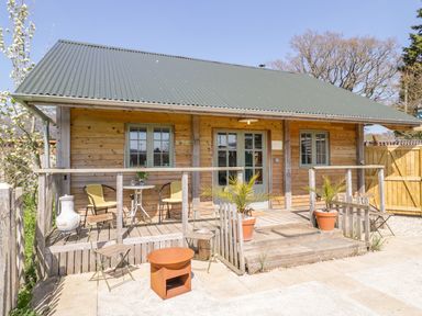 A wooden cabin with a green metal roof and a small porch with chairs and plants at Little Willow in Farrington near Child Okeford