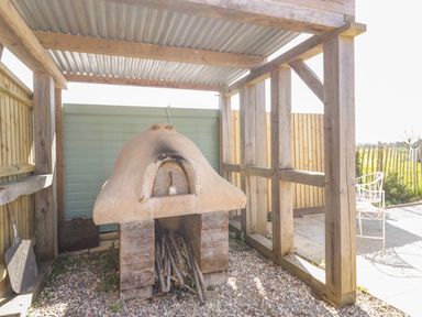 An outdoor wood-fired oven with firewood under a wooden shelter at Little Willow in Farrington near Child Okeford