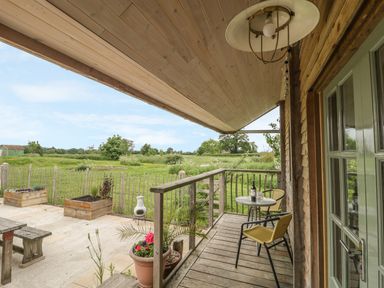 A wooden porch with two yellow chairs and a small table with a bottle and glasses overlooking a fenced grassy field at Little Willow in Farrington near Child Okeford