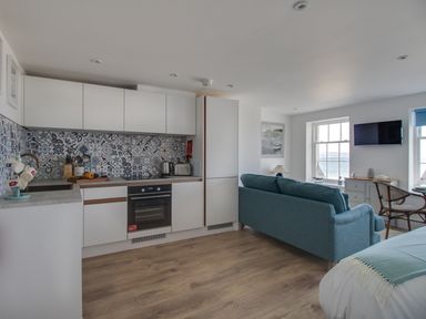 A modern kitchen and living area with a blue sofa wooden floor and a wall-mounted TV at 6 The Beaches in Weymouth