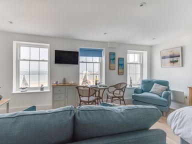 A living room with blue sofas a dining table with chairs and windows overlooking the sea at 6 The Beaches in Weymouth