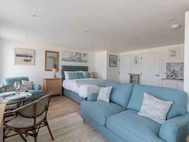 A living room with blue sofas a bed a dining table and wall art at 6 The Beaches in Weymouth