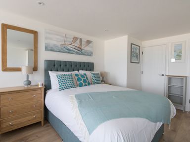 A bedroom with a bed blue headboard blue pillows and a wooden dresser with a mirror at 6 The Beaches in Weymouth