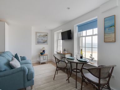 A sitting area with a blue sofa a small dining table with chairs and windows showing a beach view at 6 The Beaches in Weymouth