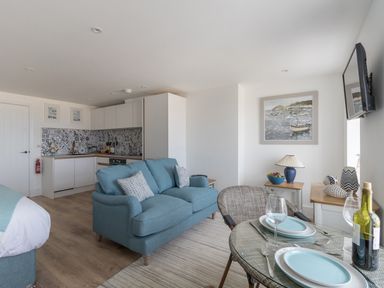 A small open plan living space with a blue sofa kitchen area dining table with plates and wine at 6 The Beaches in Weymouth