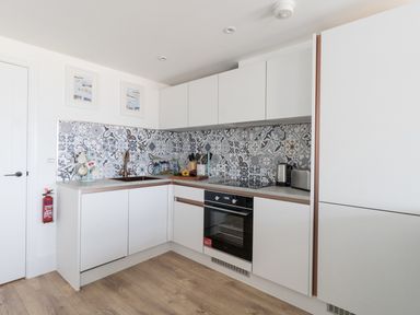 A kitchen with white cabinets patterned tile backsplash a black oven and wooden floor at 6 The Beaches in Weymouth