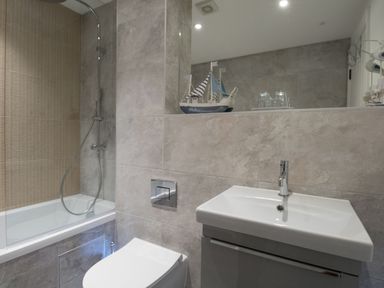 A bathroom with a bathtub shower combination a toilet a sink and a model sailboat on a shelf at 6 The Beaches in Weymouth