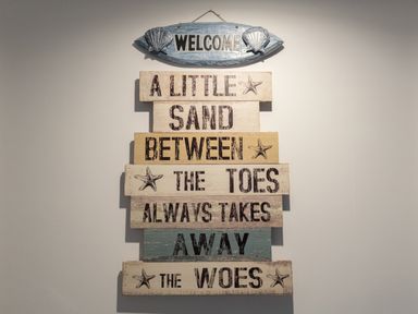 A wall decoration with a welcome sign and a wooden sign with a beach quote at 6 The Beaches in Weymouth