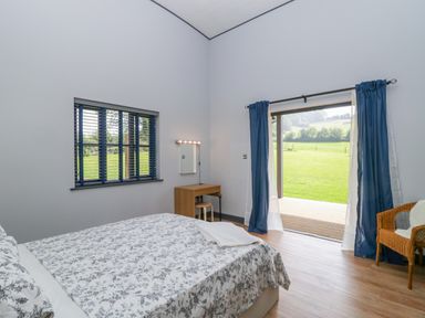 A bedroom with a bed a desk a chair and windows overlooking a garden at Bluebell in Sticklinch West Pennard Glastonbury