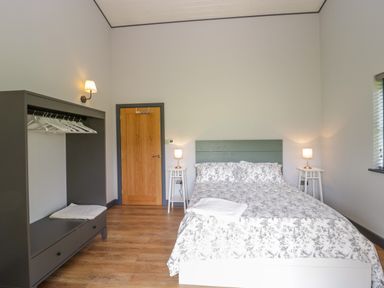 A bedroom with a bed pillows and lamps near a wooden door and an open wardrobe at Bluebell in Sticklinch West Pennard Glastonbury