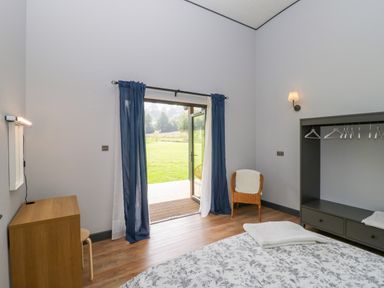 A bedroom with an open door leading outside a chair a small dresser and a bed with a floral blanket at Bluebell in Sticklinch West Pennard Glastonbury