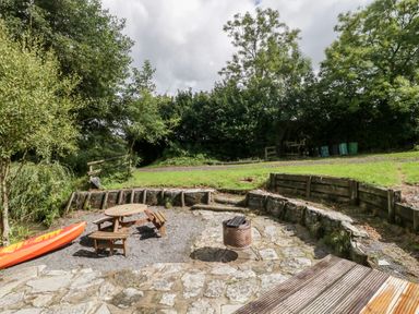 An outdoor area with a wooden picnic table a fire pit a wooden fence and a kayak near trees and grass at Bluebell in Sticklinch West Pennard Glastonbury