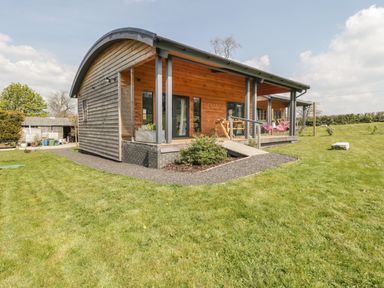 A wooden house with a curved roof and a porch in a grassy yard at Bluebell in Sticklinch West Pennard Glastonbury