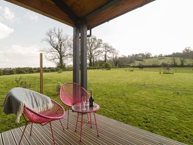 A covered patio with two pink chairs and a small table overlooking a grassy field at Bluebell in Sticklinch West Pennard Glastonbury
