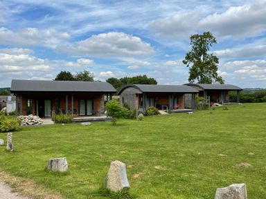 Three single-story wooden cabins with curved roofs on a grassy field under a partly cloudy sky at Bluebell in Sticklinch West Pennard Glastonbury