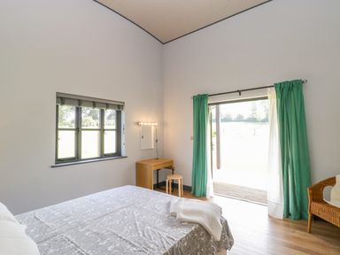 A bedroom with a bed beside a window and a door with green curtains leading outside at Primrose in Sticklinch West Pennard Glastonbury