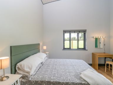 A bedroom with a bed bedside tables lamps a window and a wooden dressing table with a stool at Primrose Sticklinch West Pennard Glastonbury
