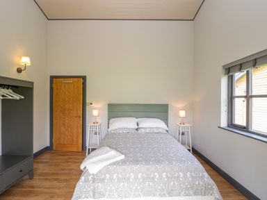 A bedroom with a double bed two bedside tables with lamps a window a wooden door and an open wardrobe at Primrose in Sticklinch West Pennard Glastonbury