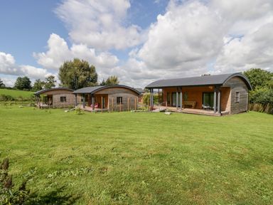 Three wooden cabins with curved roofs on a grassy field under a partly cloudy sky at Primrose in Sticklinch West Pennard Glastonbury