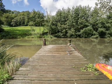 A wooden dock with metal railing extending over a pond with trees and grassy hill in the background at Primrose in Sticklinch West Pennard Glastonbury