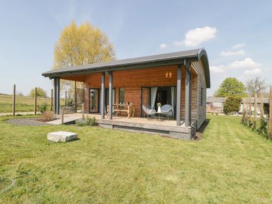 A wooden cabin with a covered porch and outdoor table and chairs in a grassy area at Primrose in Sticklinch West Pennard Glastonbury