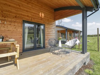 A covered wooden patio with black metal chairs and a small round table with flowers at Primrose in Sticklinch West Pennard Glastonbury