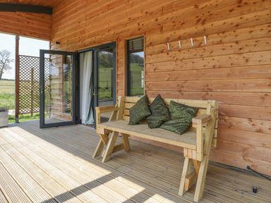 A wooden bench with green cushions on a wooden deck outside a wooden building with glass doors at Primrose in Sticklinch West Pennard Glastonbury