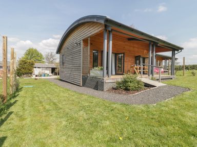 A wooden house with a curved roof and a small porch on a grassy lawn at Primrose in Sticklinch West Pennard Glastonbury