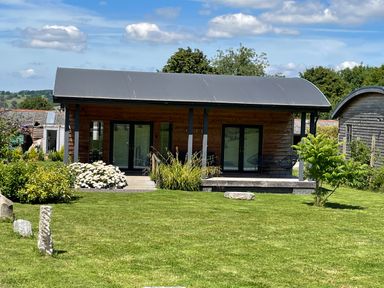A small wooden cabin with a curved roof surrounded by grass and plants at Primrose Sticklinch West Pennard Glastonbury
