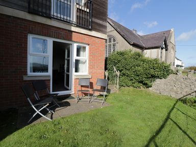 A garden area with four black folding chairs outside a brick building with an open door and window at Bay View in Benllech