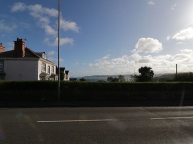 A street with houses and a hedge overlooking the sea under a blue sky at Bay View in Benllech