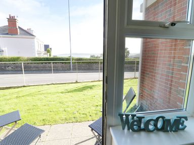 A window with a welcome sign on the sill and two chairs outside on a patio with grass at Bay View in Benllech