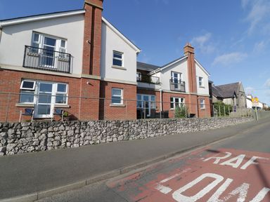A two story brick and white house with balconies and a stone wall in front and a road with RAF LON marking