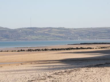 A sandy beach with rock formations in front of a body of water and hills in the background at Bay View in Benllech