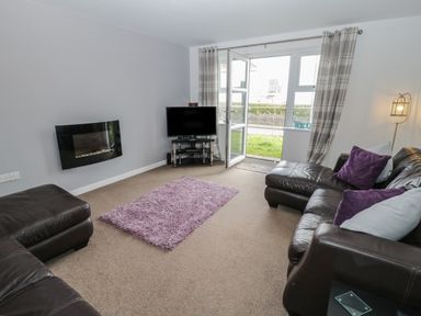 A living room with leather sofas a purple rug a wall-mounted fireplace and a TV near a glass door at Bay View in Benllech