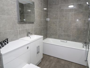 A bathroom with a bathtub sink mirror and storage cabinets at Bay View in Benllech