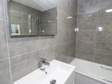 A bathroom with a white sink and tap a mirror and a bathtub with a shower at Bay View in Benllech