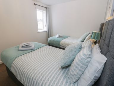 A bedroom with two single beds with striped bedding and folded towels on each bed at Bay View in Benllech