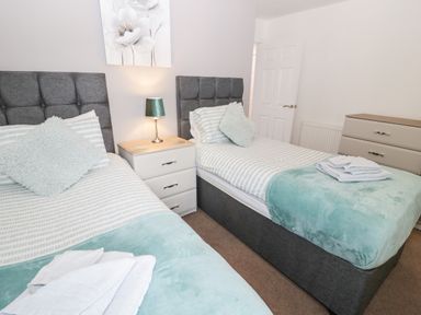 A bedroom with two single beds a bedside table with a lamp and a chest of drawers at Bay View in Benllech