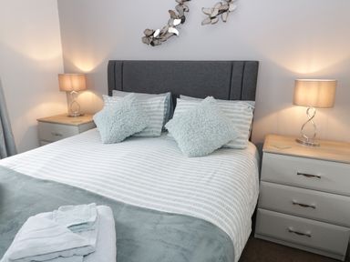 A bedroom with a bed two bedside tables lamps and folded towels at Bay View in Benllech