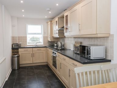 A kitchen with wooden cabinets black countertops and appliances at Bay View in Benllech
