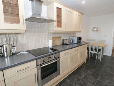 A kitchen with wooden cabinets a stove oven kettle toaster microwave and a dining table with chairs at Bay View in Benllech