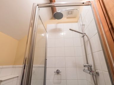 A tiled shower enclosure with a glass door and a chrome showerhead at Manor Farm Barn in Dewlish